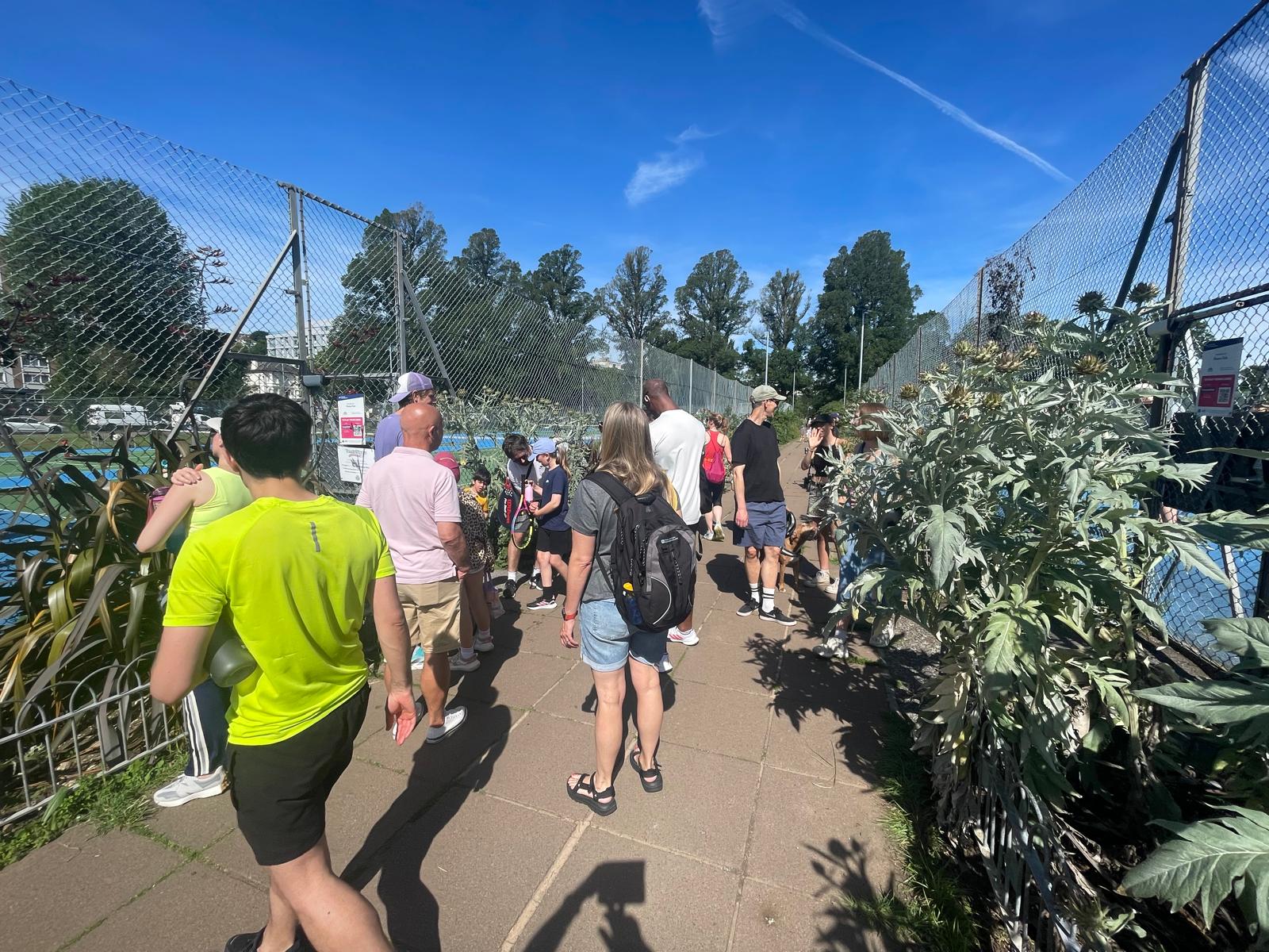 A crowd of players chatting outside the courts at Preston Park on a sunny morning